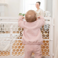Baby peaking over safety gate looking at mom