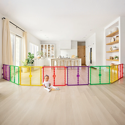 Colorful baby gate in a home with a child sitting on the floor in front of it