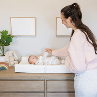 Mom holding baby's hand while they lay on the infant changing pad