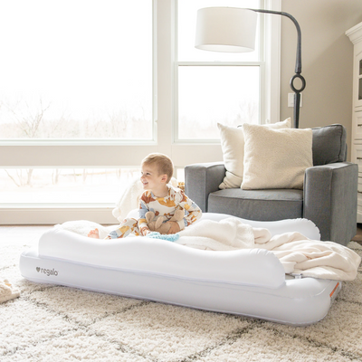 An inflatable toddler bed with white and gray colors, marked with the brand Regalo, in a room set up for a child to sleep on it.