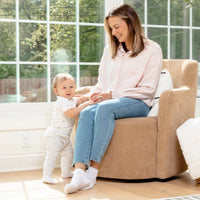 Baby standing by mom who's sitting on chair