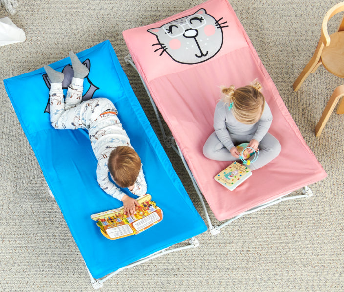 Lifestyle photo of two children playing on two MyCot beds in a living room, showing pink and blue variations