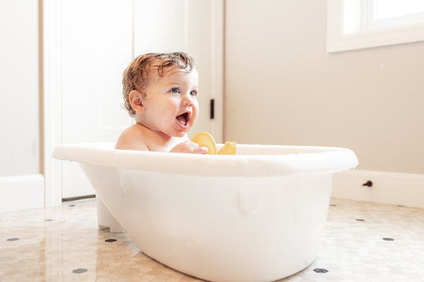Happy baby plays in the Baby Basics™ Grow with Me Baby Bath Tub side view