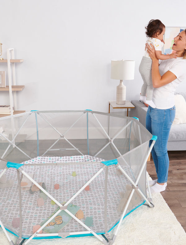 Holding baby next to 8-panel My Play Portable Play Yard® with Pad