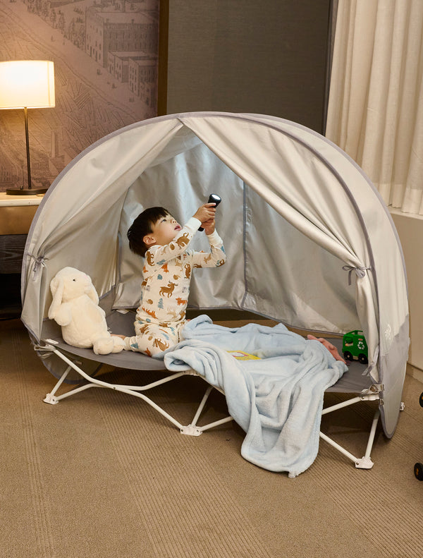 Child holding flashlight while on My  Cot® with Canopy Portable Toddler Bed™