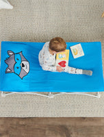 Child looking at books on blue raccoon My Cot® Pals Portable Toddler Bed